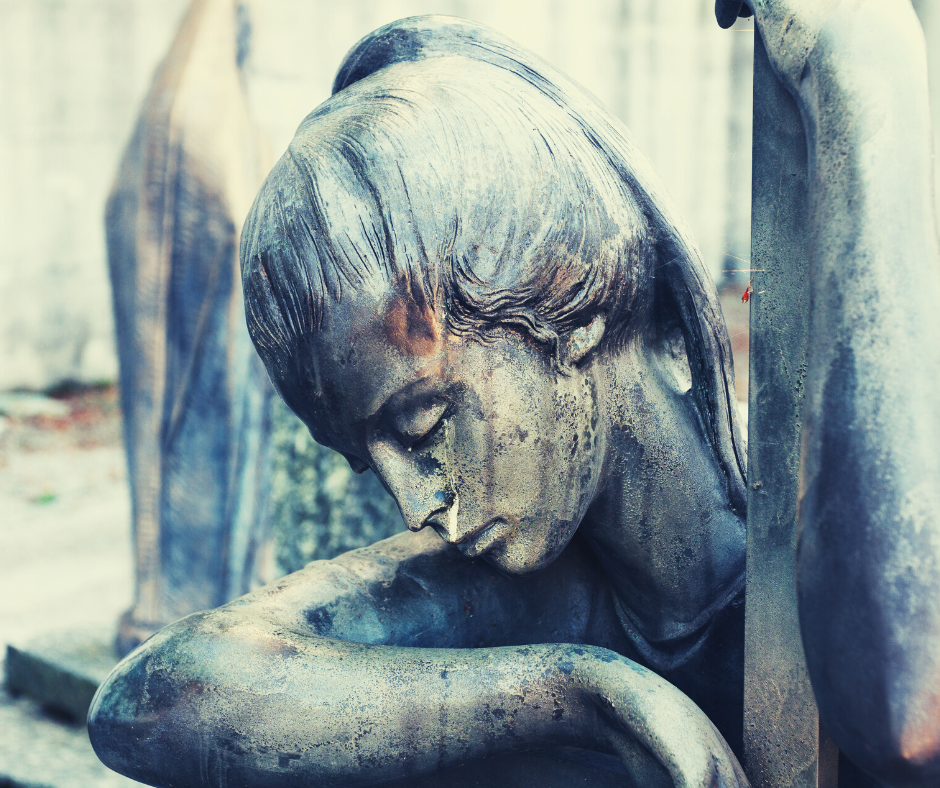 Headshot of an weather beaten bronze statue of an angel weeping.