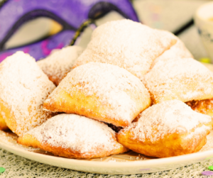 A plate of beignets with a Mardi Gras purple mask in the background.